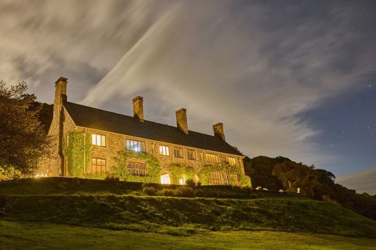 a view of bossington hall at night, with lights glowing under a Aurora Borealis sky