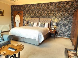 A view of a B&B room with a super king bed and a William Morris style wallpaper.